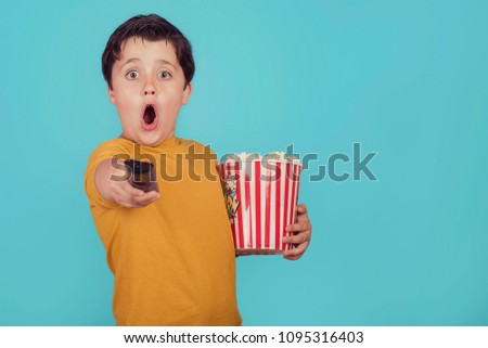 surprised boy with popcorn and television remote control on blue background