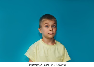 A Surprised Boy With Wide Eyes Boy In A Yellow T-shirt On A Blue Background. Portrait Of A Child, Front View, Copy Space