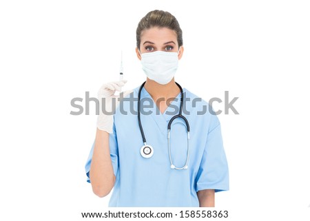 Surprised brown haired nurse in blue scrubs wearing protection mask and holding a syringe on white background