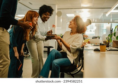 A surprised businesswoman is having a birthday surprise at the office from colleagues. A diverse coworkers bringing a birthday cake to businesswoman and surprising her. Birthday celebration at office. - Powered by Shutterstock