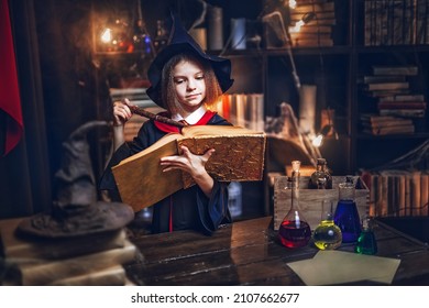 Surprised caucasian little girl in witch Cosplay reads magic book while holding magic wand, Halloween costume. Halloween party. - Shutterstock ID 2107662677
