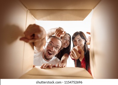 The Surprised Caucasian Man And Women Opening Carton Box And Looking Inside. The Package, Delivery, Surprise, Gift, Lifestyle Concept. The Smiling People Pointing To Camera