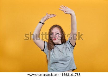 Surprised cheerful young woman in casual shirt, looking camera, spreading hands over head isolated on orange background in studio. People sincere emotions, lifestyle concept.