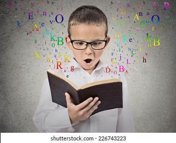 Surprised child reading a book with letters flying away from it isolated on grey wall background. Face expression. Education concept