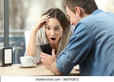 Surprised couple meeting in a coffee shop watching media content in a smart phone 