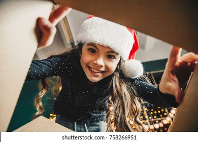 Surprised Cute Child Girl Opening A Christmas Present. Little Kid Having Fun Near Decorated Tree Indoors.  Happy  Holidays And New Year.