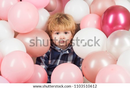 Surprised emotions, surprised child looks at the camera on a background of pink and white balloons. Beautiful baby face, portrait of a beautiful child. Attractive boy with big eyes. Birthday party