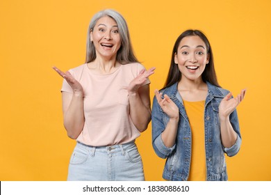 Surprised Excited Funny Shocked Family Two Asian Women Gray-haired Mother Brunette Daughter In Casual Clothes Keeping Mouth Open Spreading Hands Isolated On Yellow Color Background Studio Portrait