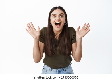 Surprised And Excited Girl Screaming From Joy And Happy News, Raising Hands Up, Staring At Camera Pleasantly Astounded, Standing Against White Background