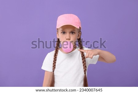 Surprised girl blowing bubble gum on purple background