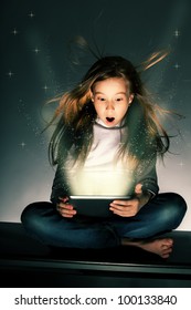 Surprised Girl Looking At A Magic Tablet. Child With Tablet Computer