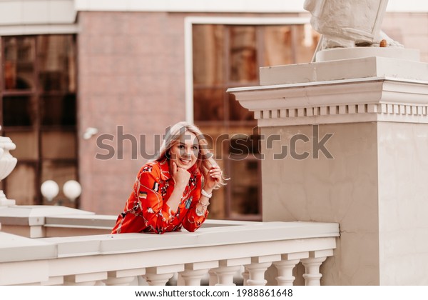 surprised girl on\
the street terrace looks and smiles. Blonde girl in Europe on the\
balcony. Lovely girl with curly hair waving walking down the street\
and looking around with\
smile.