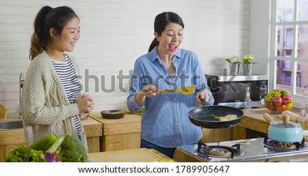 Surprised girls look at hot pan while cooking delicious meal in the morning. shocked woman laughing flip egg and having fun. happy female friends preparing breakfast together with positive emotion