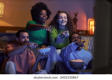 Surprised group of friends watching movie together and pointing at TV screen together in dark living room - Powered by Shutterstock