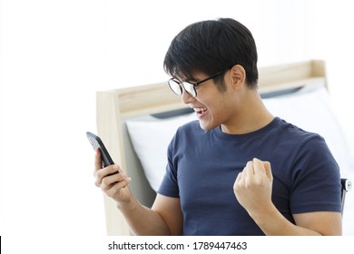 Surprised Happy Asian Man Using Mobile Phone On Desk Read Good News On Internet, Amazed Asian Guy Winner Excited Win Scream With Joy Celebrate Victory Success At Home. WORK FROM HOME Concept. 