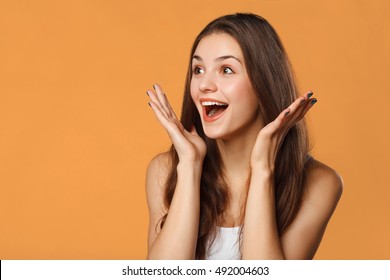 Surprised happy beautiful woman looking sideways in excitement. Isolated on orange background - Shutterstock ID 492004603