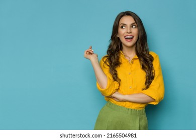 Surprised and happy beautiful young woman in linen shirt and shorts looking to the side and talking. Three quarter length shot against blue background. - Shutterstock ID 2165504981
