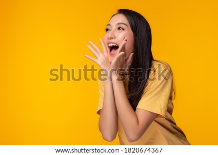 Surprised happy beauty asian woman looking copy space in excitement. Expressive facial expressions. Presenting some product. Beautiful girl act like a telling secret Isolated on yellow background