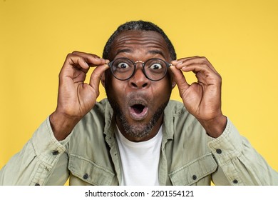 Surprised Happy Funny Excited Mature Black Male In Casual And Glasses With Open Mouth Look At Camera, Isolated On Yellow Background, Studio, Close Up. Emotions, Facial Expression, Great Ad And Offer