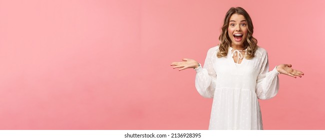 Surprised and happy young blond girl realise she won, receive really good news, spread hands sideways smiling and look amazed at camera, standing pink background lucky and upbeat