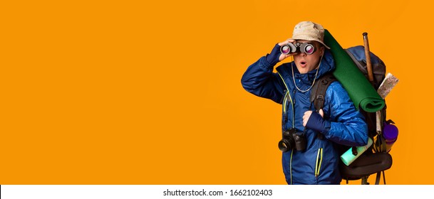 Surprised hiker with big backpack using binoculars, yellow background, panorama with copy space - Powered by Shutterstock