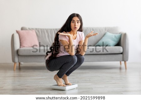 Surprised Indian lady sitting on scales, cannot understand lack of weight loss at home, copy space. Millennial Asian lady shocked over result of slimming diet. Healthy living concept