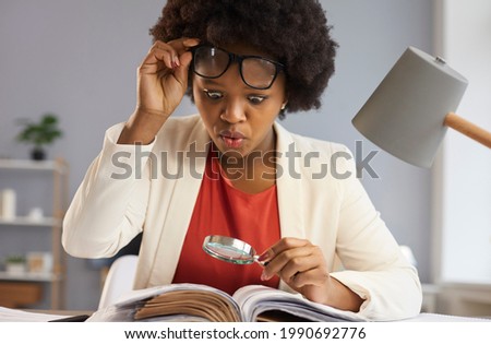 Surprised inquisitive black woman with magnifying glass takes off glasses as she sees an amazing curious fact in the book she's reading. Shocked financial advisor studying business documents in office