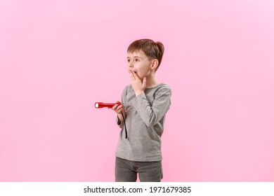 Surprised little boy with flashlight on color background