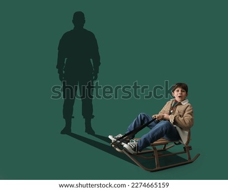 Surprised little boy with sledge and silhouette of soldier on green background