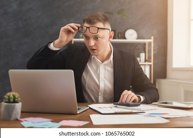 Surprised Male Financial Advisor Working With Papers And Laptop At Modern Office Interior. Shoked Man In Formal Wear Checking Documents, Seeing Unexpected Growth, Copy Space