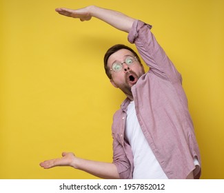 Surprised man in glasses shows a large size with hands, he exaggerates and looks at the camera in amazement. Copy space. 