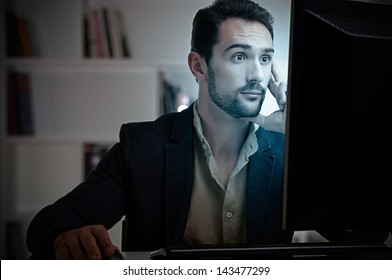 Surprised man looking at a computer screen, in a dark room