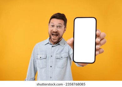 Surprised man showing smartphone in hand on yellow background - Shutterstock ID 2358768085