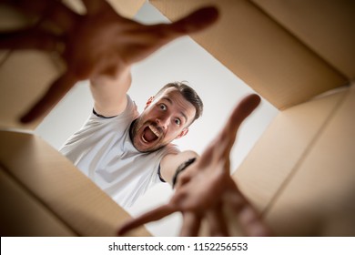 The Surprised Man Unpacking, Opening Carton Box And Looking Inside. The Package, Delivery, Surprise, Gift Lifestyle Concept. Human Emotions And Facial Expressions Concepts