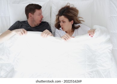 Surprised Man And Woman Looking Under Covers While Lying In Bed