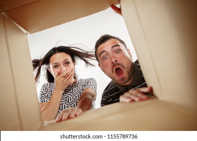 The Surprised Man And Woman Unpacking, Opening Carton Box And Looking Inside. The Package, Delivery, Surprise, Gift And Lifestyle Concept