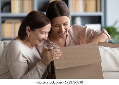 Surprised middle aged mother and adult daughter unpacking parcel together, looking in cardboard box, happy young woman with mature mum excited by delivery, received online store order