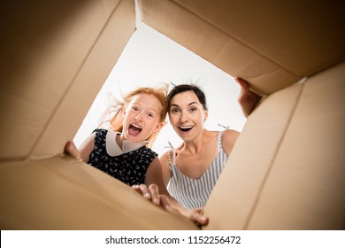 The Surprised Mom And Daughter Unpacking, Opening Carton Box And Looking Inside. The Package, Delivery, Surprise, Gift Lifestyle Concept. Human Emotions And Facial Expressions Concepts