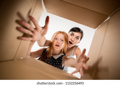 The Surprised Mom And Daughter Unpacking, Opening Carton Box And Looking Inside. The Package, Delivery, Surprise, Gift Lifestyle Concept. Human Emotions And Facial Expressions Concepts