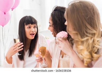 Surprised Multicultural Girls Having Fun With Champagne And Cupcake During Bachelorette Party With Pink Balloons