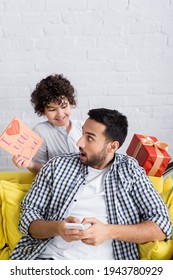 Surprised Muslim Man Near Cheerful Son Holding I Love You Dad Card And Gift Box