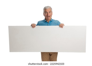 Surprised Old Man Holding Empty White Board And Showing It While Standing And Presenting On White Background In Studio