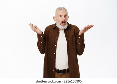 Surprised Old Man, Senior Caucasian Guy Shrugging Shoulders And Looking Amazed At Camera, Standing In Disbelief Against White Background