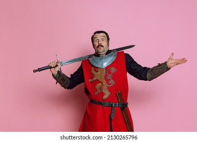 Surprised. One Young Man, Medieval Warrior Or Knight Wearing Wearing Armor Clothing Posing Isolated Over Pink Background. Model With Wounded Face. Comparison Of Eras, History, Funny Meme Emotions