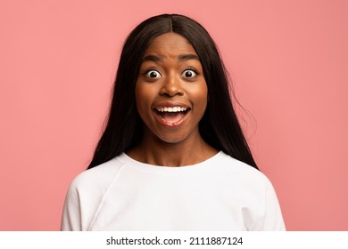 Surprised pretty african american millennial woman in white looking at camera with eyes and mouth wide open, posing alone on pink studio background, closeup shot, copy space. Human emotions concept