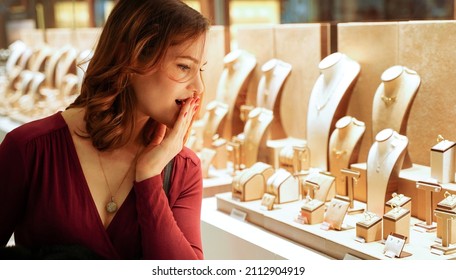 Surprised Pretty Woman Looking At Jewelry In Store Window. Girl Near Jewellery. Interested Customer Chooses Gold, Diamonds Or Precious Stones. Purchaser