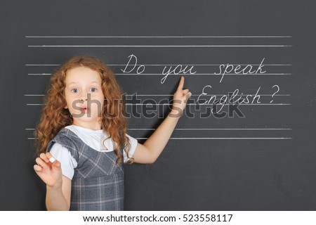 Surprised redhead girl asks a question -  Do you speak English, stand near blackboard in the classroom. Education concept.