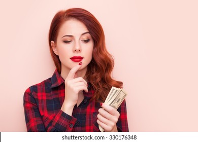 Surprised redhead girl in red tartan dress with money on pink background. - Shutterstock ID 330176348