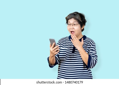 Surprised Senior Asian Woman Holding And Looking Smartphone On Isolated Background Feeling Surprised And Amazed. Older Female Lifestyle Concept  Blue Background.