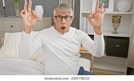 Surprised senior man in glasses making funny face with ok signs in a modern bedroom - Powered by Shutterstock